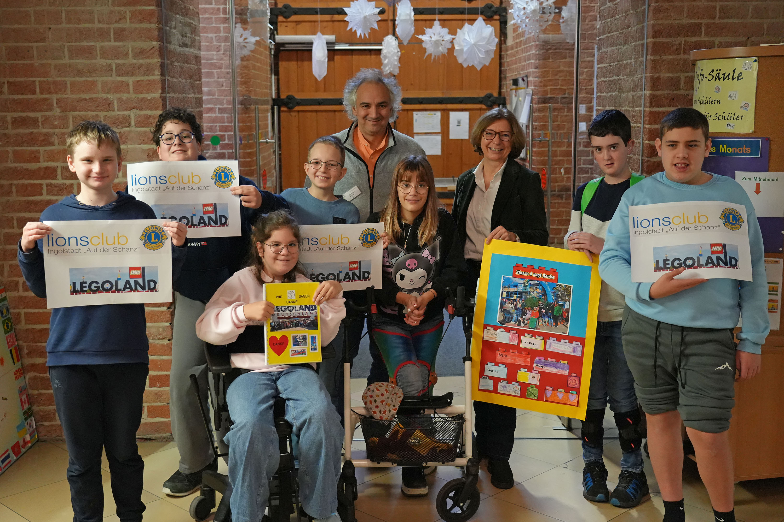 Gruppenfoto: Schülerinnen und Schüler der Johann-Nepomuk-Kurz-Schule halten Dankeschön-Plakate und Lions-Club-Schilder mit dem Legoland-Logo in die Höhe, dahinter Schulleiter Harald Christmann und Lions-Präsidentin Maria Garnisch.
